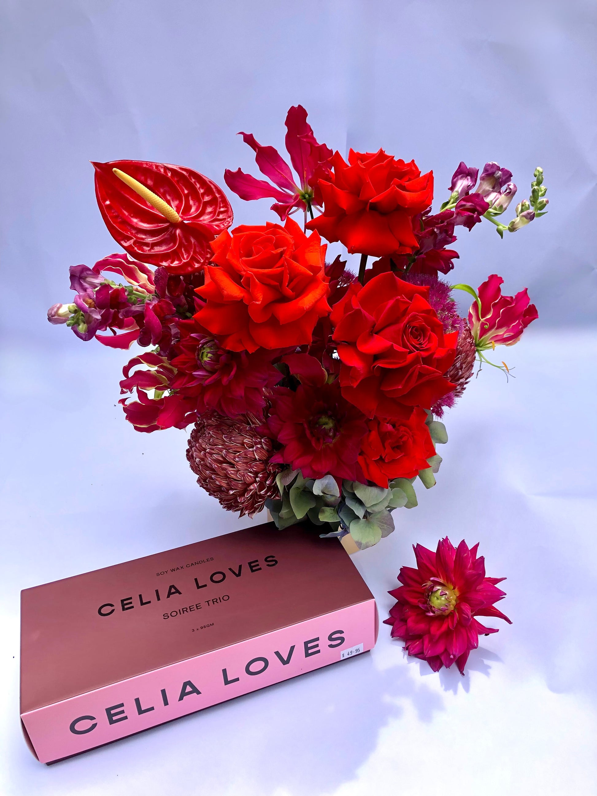 A lively floral display titled "A Soiree Affair Red Bouquet" from Flowers on Norton St showcases a mix of red and burgundy flowers, including red roses and anthuriums, arranged in a vase. A pink box labeled "Celia Loves" sits nearby with a single red flower adorning the white surface.