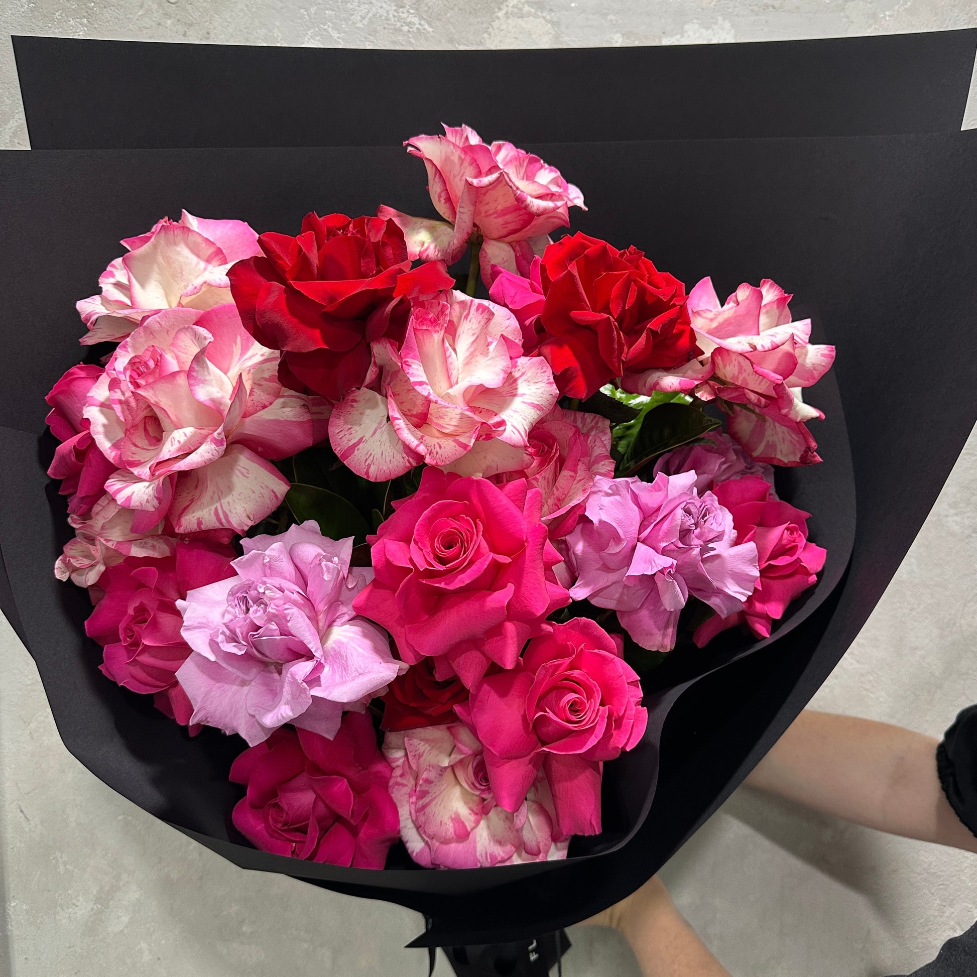 The Rose Trio Bouquet by FlowersonNortonSt features handcrafted Colombian roses in red, pink, and white, wrapped in elegant black paper. The delicate petals with a stunning color blend create an elegant and striking gift.