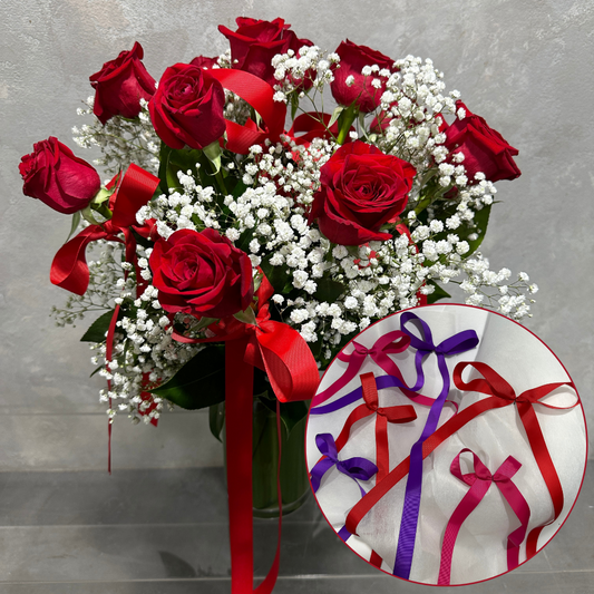 The Add on Bows by Flowers on Norton St features a bouquet of red roses and white baby's breath with red ribbons and bows, elegantly arranged in a clear vase. A circular inset highlights vibrant red, purple, and pink bows against a white background.