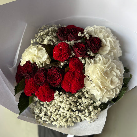 The "A Cloud of Love Mixed Bouquet" by Flowers on Norton St features red roses, white hydrangeas, red carnations, and baby's breath elegantly arranged in white wrapping paper.