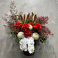 The "Aussie Christmas Vase" by Flowers on Norton St beautifully captures the essence of holiday cheer with its floral arrangement of red roses, white orchids, and white chrysanthemums, complemented by Australian native Christmas bush and greenery. The dark leaves and small red branches are elegantly displayed in a dark vase against a light gray textured wall.