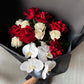 The Red and White Bud + Bloom Rose Bouquet by Flowers on Norton St features roses and white orchids elegantly wrapped in black paper. This 12-rose bouquet is beautifully arranged on a light gray surface, embodying classic charm.