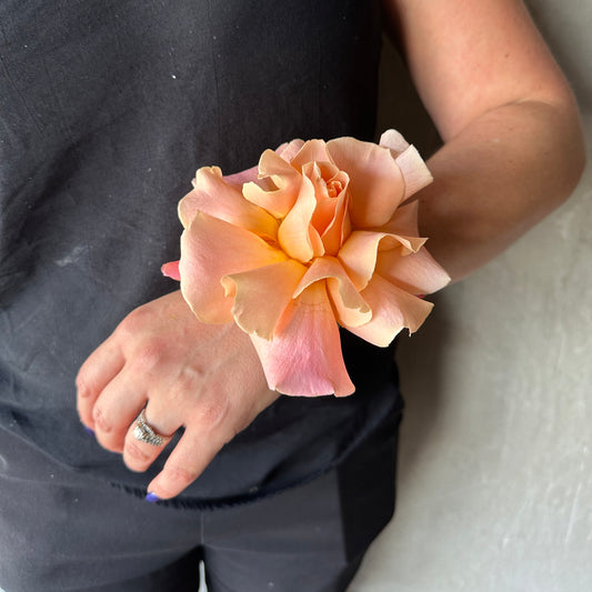 A person adorned in a black shirt holds a gorgeous arrangement reminiscent of the Modern Wrist Corsage from Flowers on Norton St, featuring stunning orange and pink roses perfect for school formals. The open flower reveals its intricately layered petals, with a ring elegantly displayed on the person's finger.