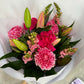 Introducing the "Watermelon Crush" by Flowers on Norton St: a vibrant Mother's Day bouquet featuring pink lilies, roses, and carnations accented with snapdragons and lush green leaves. The flowers are beautifully arranged to showcase stunning shades of pink blooms against a pristine white background.