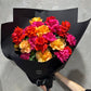 The Rose Trio Bouquet by FlowersonNortonSt features vibrant handcrafted roses in red, pink, orange, and yellow. Elegantly wrapped in black paper, these stunning blooms are set against a gray textured background.