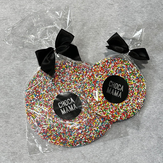 Two cellophane-wrapped CHOCAMAMA Giant Chocolate Freckles topped with colorful sprinkles sit on a gray surface, each decorated with a black bow and labeled with Flowers on Norton St, making them an irresistible treat for kids.