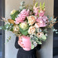 Adorned in black, an individual holds a large Winter Garden Vase by Flowers on Norton St, overflowing with a vibrant bouquet of roses, snapdragons, ornamental kale, and native foliages. The pink, cream, and green hues form a lush arrangement against a neutral backdrop.