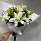 The Rose-lily Bouquet from FlowersonNortonSt features a fragrant assortment of white lilies and rose-lilies, elegantly presented with their buds wrapped in delicate white paper. The arrangement is set against a subtle gray background, highlighting its timeless beauty.