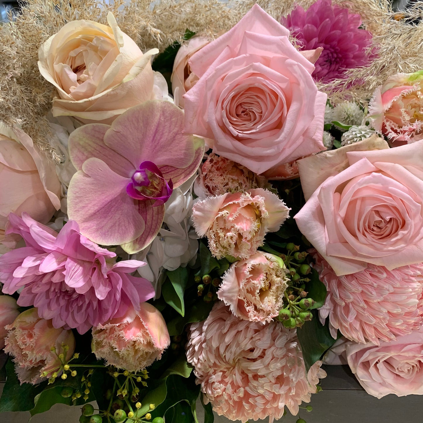 A detailed look at the Florist Choice bouquet from Flowers on Norton St showcases pink roses, an orchid, and a mix of other pink and white blooms with lush green foliage. The flowers come in gentle, pastel shades, forming a delicate and sophisticated arrangement ideal for flower delivery in Sydney.