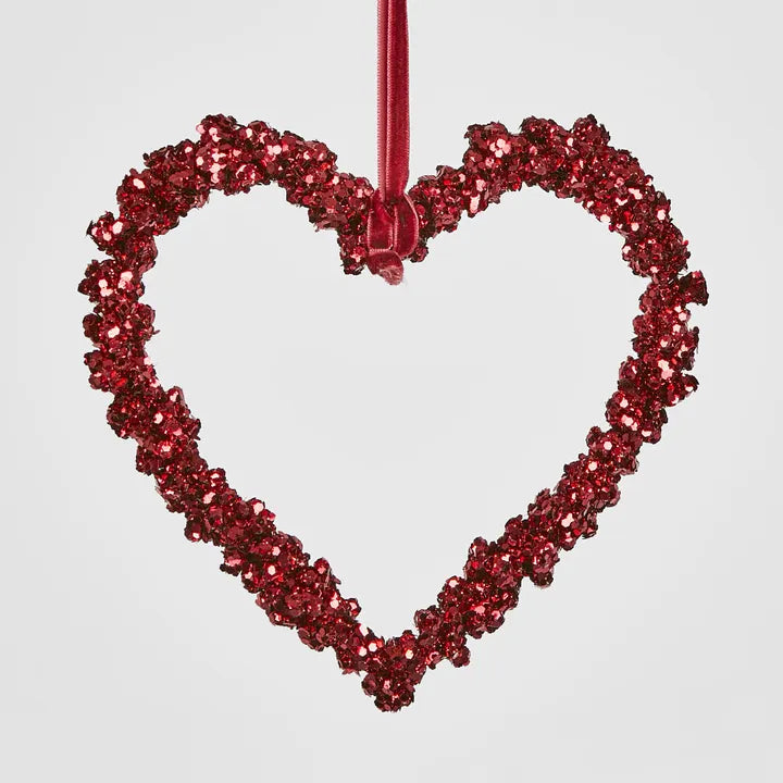 A Shimmer Hanging Heart Ornament from Flowers on Norton St in red glistens by a ribbon against a plain background, infusing your festive decorations with elegance.