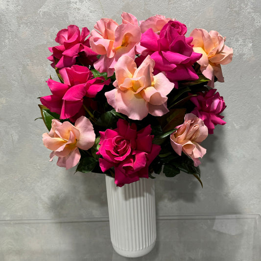 The Reflexed Rose Vase by Flowers on Norton St features a bouquet of vibrant pink and peach Colombian roses set against a textured gray background. The fresh and lush flowers create an appealing contrast with the white ceramic vase.