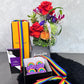 The Rainbow Pride arrangement from Flowers on Norton St showcases a vibrant display of multicolored flowers in a vase, complemented by a Veuve Clicquot champagne box, a chocolate box, and rainbow cupcakes adorned with purple frosting and rainbow toppers. A graceful rainbow ribbon drapes over the entire setup to celebrate Pride Month.