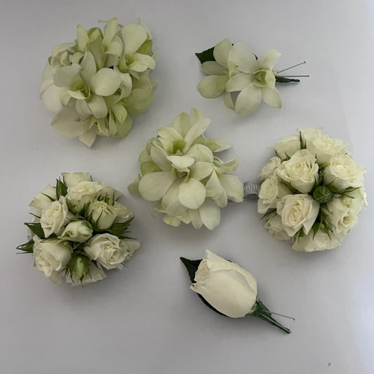 The Classic Wrist Corsage by Flowers on Norton St features six small floral arrangements with white roses and orchids, placed against a plain background. These elegant round bouquets and single stem flowers are perfect for adding a touch of grace to school formals or serving as a delicate accessory.