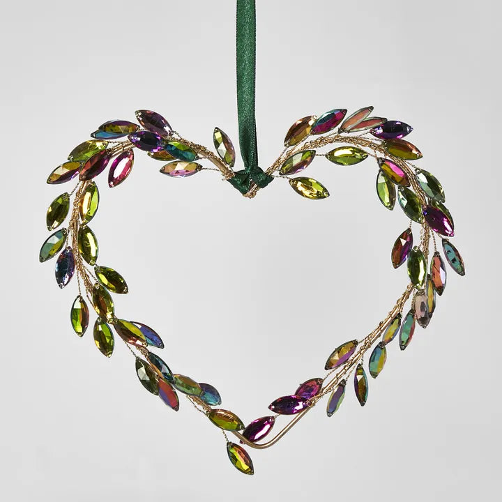 The Crowne Gem Hanging Heart Ornament by Flowers on Norton St is a festive decorative piece shaped like a heart, crafted from colorful, iridescent leaves arranged on delicate wire. It hangs gracefully from a green ribbon, adding holiday cheer to any setting, much like an ornament on a Christmas tree.