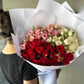 A person holds a stunning Mini Roses Enmasse Bouquet from Flowers on Norton St, elegantly wrapped in white paper against a gray backdrop. The bouquet's charm and romance shine as the individual, wearing a black shirt, faces away.