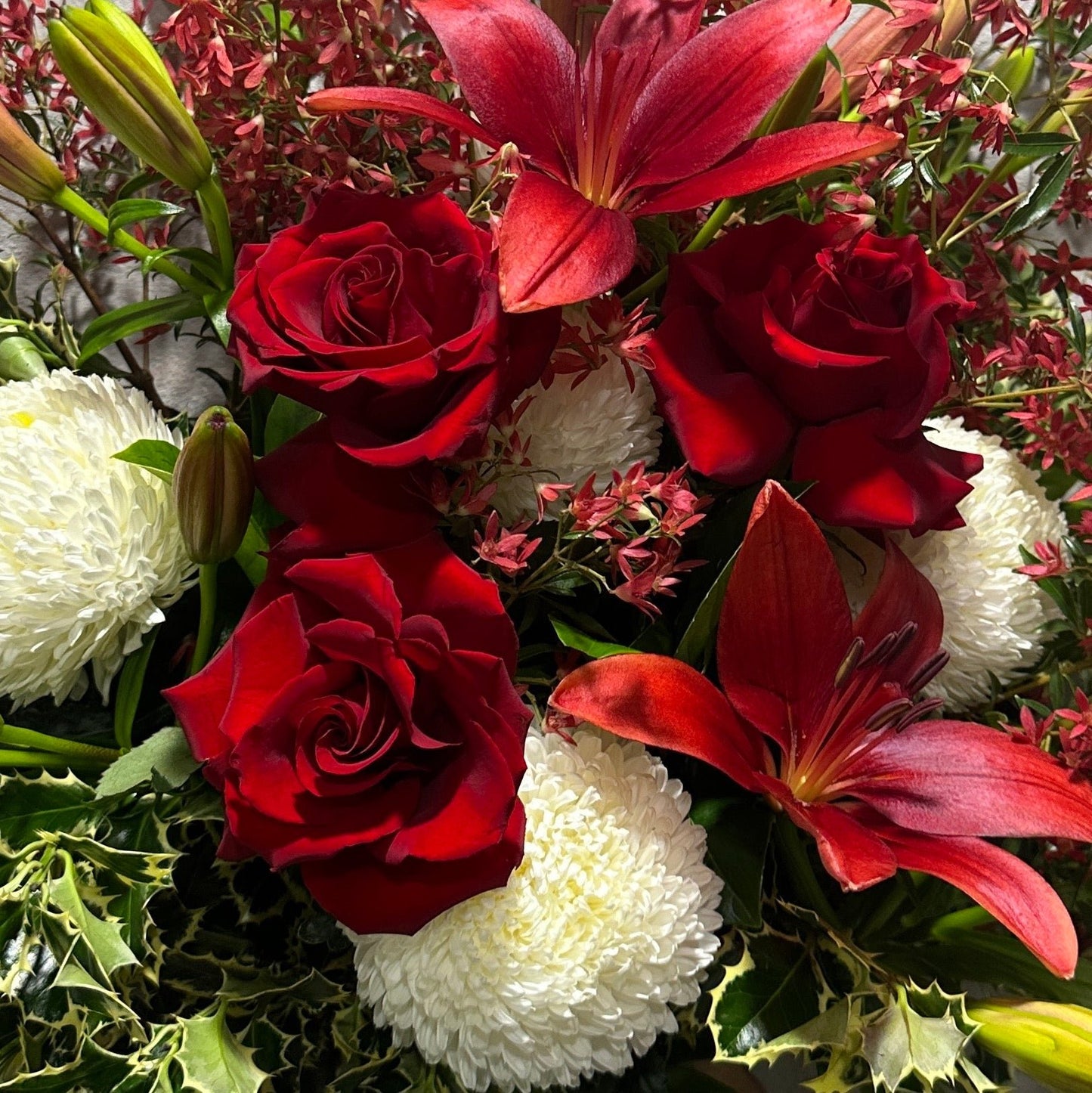 The Florist Choice - Festive bouquet from Flowers on Norton St features vibrant red roses, striking red lilies, and elegant white chrysanthemums nestled among lush green foliage. This artful arrangement offers a captivating contrast of colors and textures, ideal for anyone looking for affordable flower delivery in Sydney.