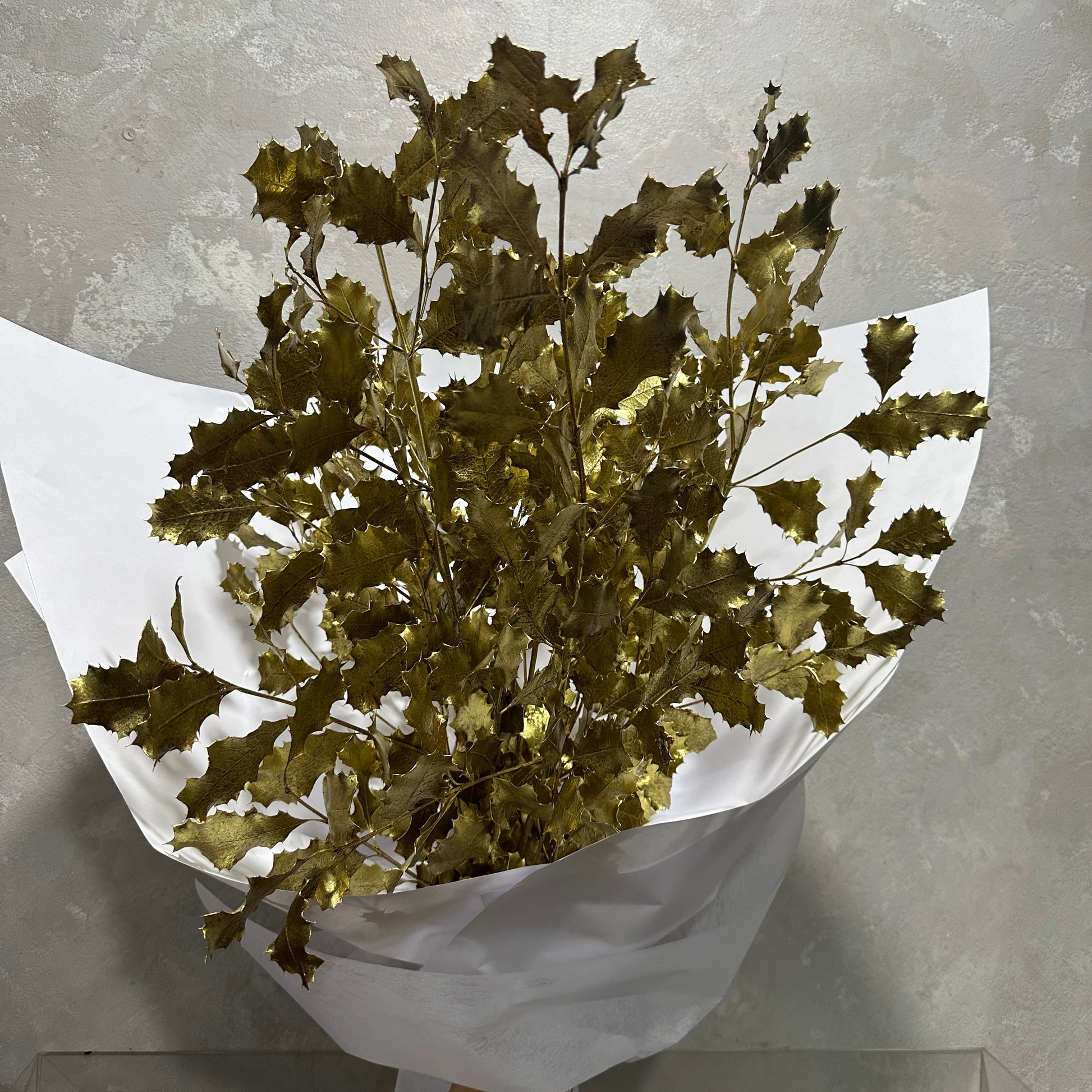 A bouquet from Flowers on Norton St featuring Dried Gold Xmas Foliage, elegantly wrapped in white paper against a gray background.