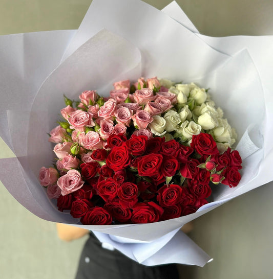 The Mini Roses Enmasse Bouquet from Flowers on Norton St features a large, artfully clustered mix of vibrant red, pink, and white blossoms wrapped in white paper for a colorful and fresh display.