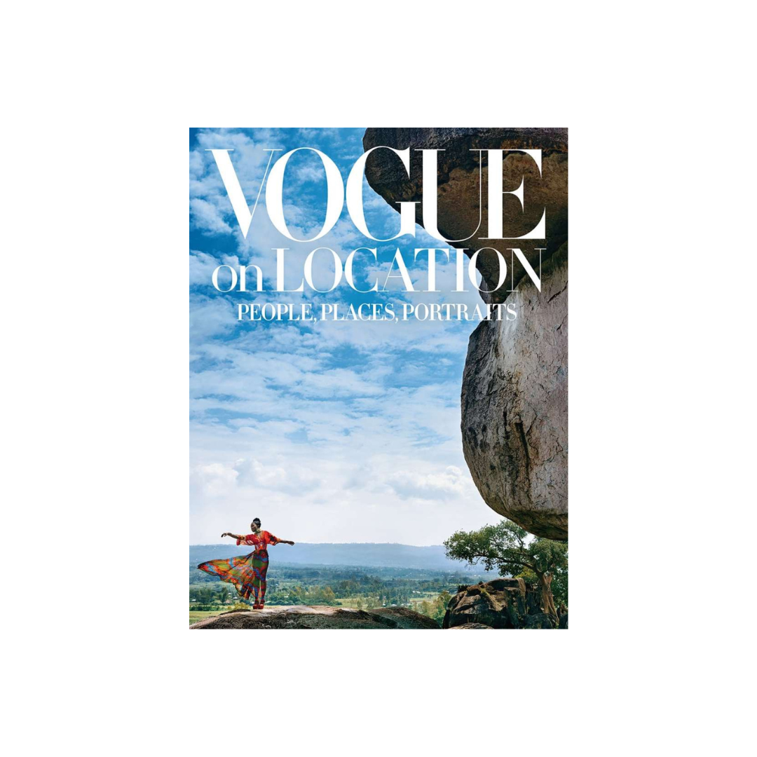 The cover of "Vogue on Location" by FlowersonNortonSt encapsulates the spirit of travel fashion, featuring an individual in vibrant clothing posing near a large rock formation with arms outstretched. The backdrop presents a landscape with a blue sky and scattered clouds, reminiscent of classic reportage style.