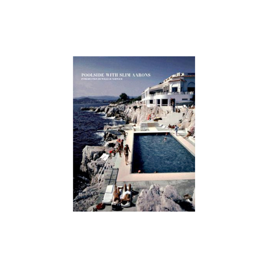 Capture a stylish retro photograph with "Poolside with Slim Aarons" by FlowersonNortonSt. This idyllic scene features a luxury seaside pool, lounge chairs, and sunbathers, set against a dramatic rocky coastline and clear blue sky. A grand white building serves as the perfect backdrop for your moments by the pool.