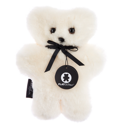 The Flatout Bears Baby Toy by Flowers on Norton St is a fluffy white teddy crafted from Australian sheepskin. It features a black ribbon and a "FLATOUTbear" tag. With small black eyes, nose, and outstretched arms, it's the perfect comfort companion ready for hugs.