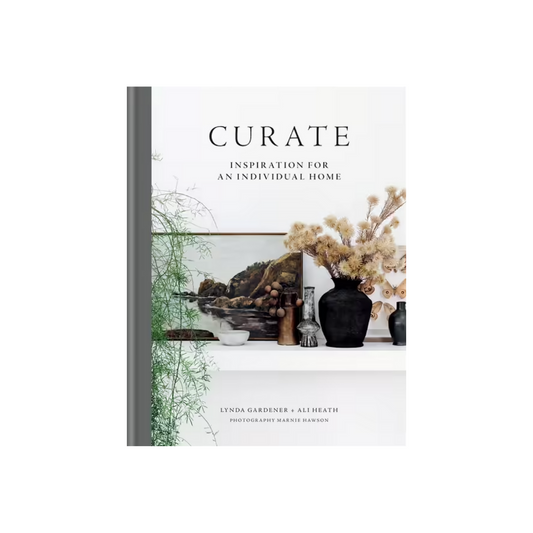 The image shows the book cover of "Curate: Inspiration for an Individual Home" Gift Book by FlowersonNortonSt, authored by Lynda Gardener and Ali Heath. Featuring a minimalist design, it embodies home styling with nature-themed photos and decorative items like vases and dried flowers.