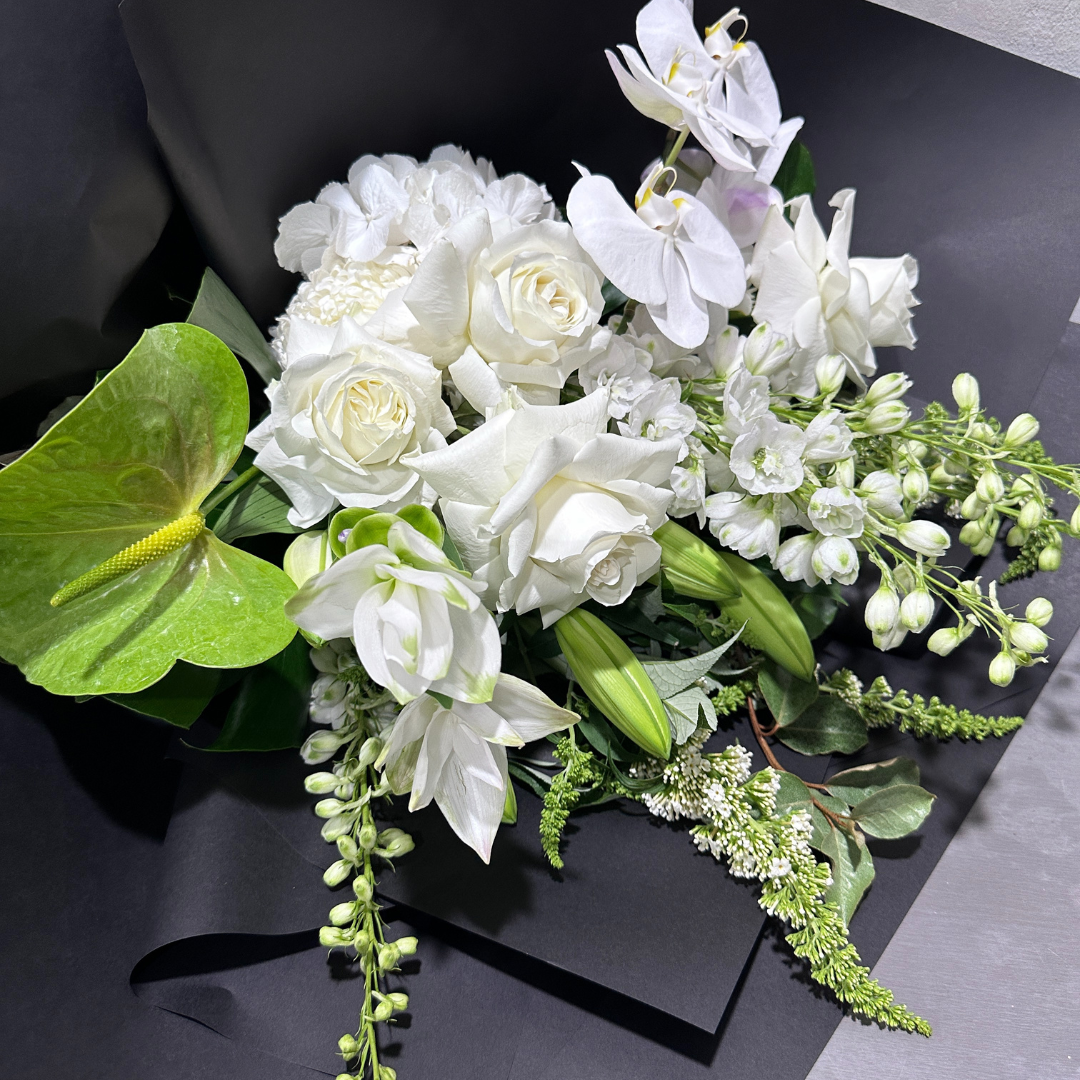 The Under the Limelight bouquet by Flowers on Norton St features an arrangement of white roses, orchids, and lilies with a botanical twist of lime anthuriums and other greenery against a black background.