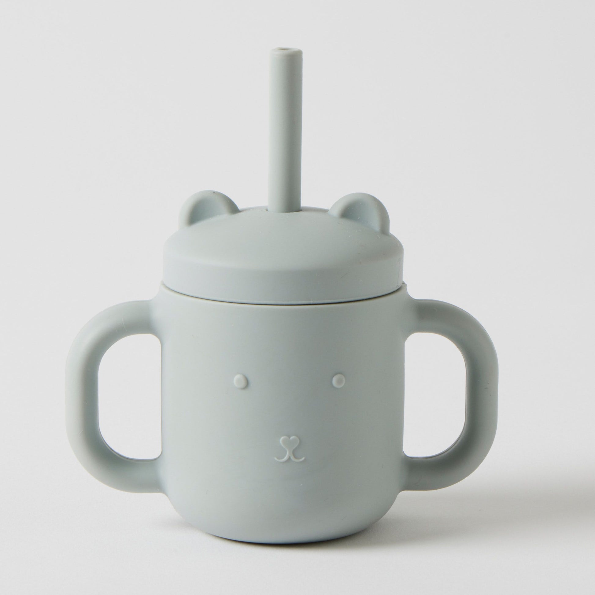 The Silicone Sippy Cup with Straw by Flowers on Norton St is available in light blue and includes two handles along with a built-in straw. It features an adorable bear face design with embossed ears on the lid and is made from non-toxic, BPA-free material to ensure your child's safety and enjoyment.