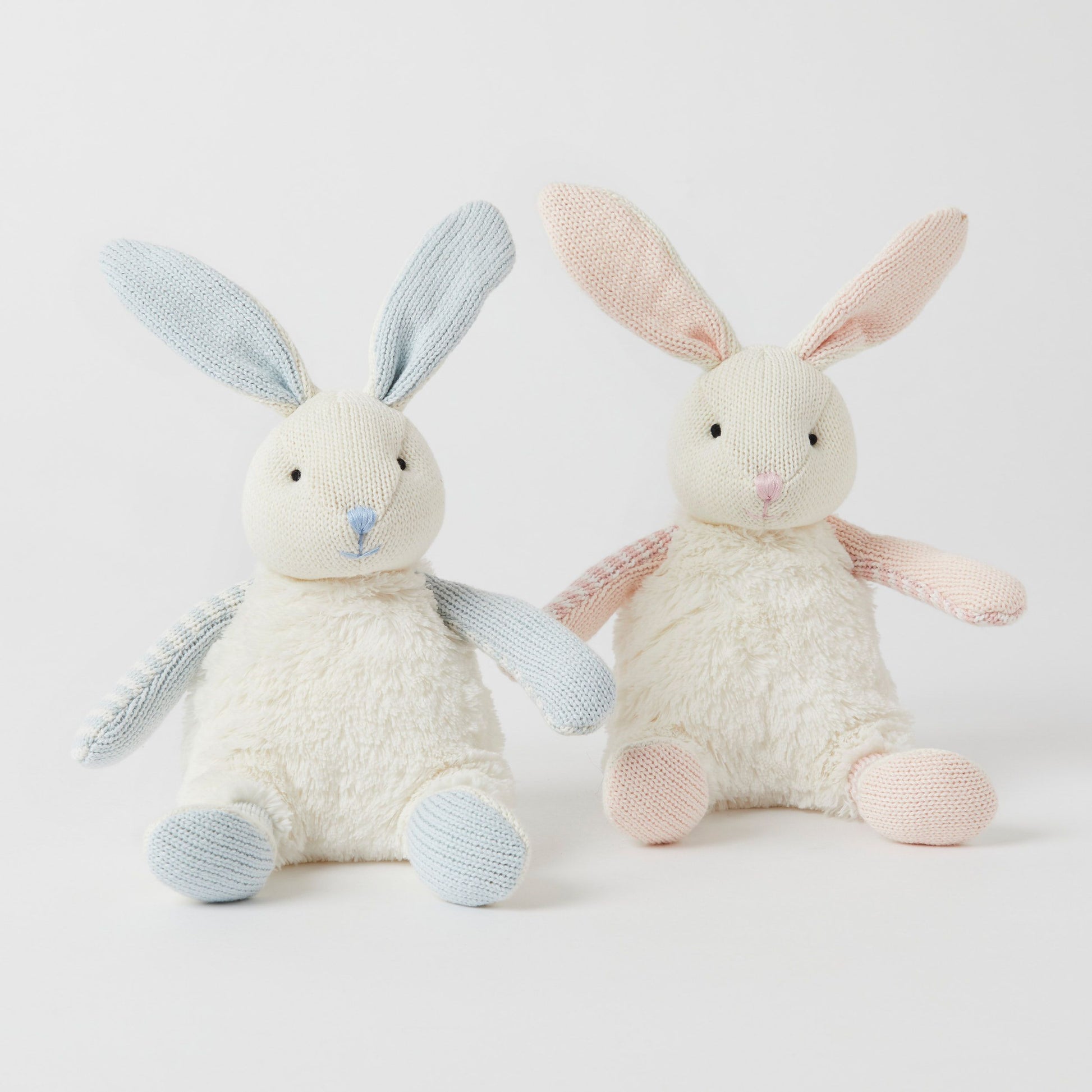 Against a white background, two Baby Bunnies from FlowersonNortonSt sit cuddling. One bunny features blue ears and feet, while the other is adorned with pink accents. Both have ultra-soft cotton bodies and embroidered facial details, making them perfect for snuggling.